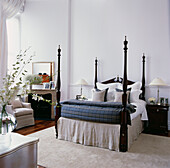 Four poster bed dressed with bed linen in large white bedroom with fresh flowers