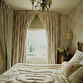Soft flowery and chequered drapes around double bed with eiderdown