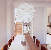 Modern open plan dining room with large white multi shade ceiling light above long dining table with plywood chairs