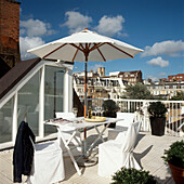 Weißer Tisch, Stühle und Sonnenschirm auf einer Dachterrasse