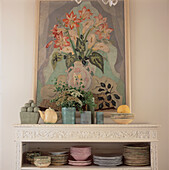 Pastellfarbenes Geschirr auf einer dekorativen Anrichte vor einem Gemälde mit Amaryllisblüten