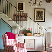 Gepolsterter Sessel mit Karomuster in einem Wohnzimmer mit Treppe und Kronleuchter