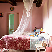 Children's bedroom in soft pink tones with floral pink quilts and mosquito nets hung from the ceiling