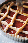 Brushing the pastry lattice of a quince jam tart with egg and milk