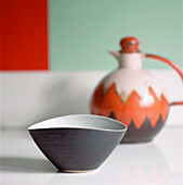 Lucie Rie ceramic bowl and colourful decanter displayed against a boldly coloured wall on a white lacquered sideboard 