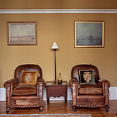 Two worn leather vintage armchairs in living room with yellow painted walls
