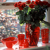 Red coloured glass vases on window sill with red roses 