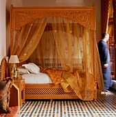 Verziertes und dekoratives goldfarbenes Schlafzimmer mit Himmelbett mit goldener Bettwäsche und Voile-Vorhängen mit gefliestem Mosaikboden im Hotel Riad Myra in Fez, Marokko
