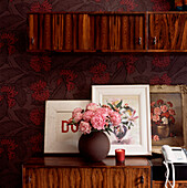 Still life with paintings floral wallpaper dark wood units and pink flowers