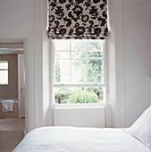 View across white bed to open sash window and radiator with view through to en suite bathroom