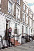 Exterior of row of Victorian London townhouses with young woman closing the door