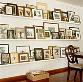 A collection of framed family photos are displayed on narrow white shelves across the wall in the dining room
