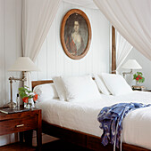 Four poster bed in the master bedroom with crisp white bed linen and a vintage portrait painting 