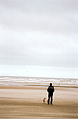 Man and dog looking out to sea on the beach 