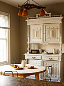 Weiße dekorative Vintage-Kommode in der Wohnküche mit rundem Tisch und Stühlen und Radio