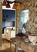 View in to the kitchen with wallpapered partition wall with built in fish tank and vintage work bench with rustic pottery collection