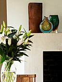 Detail of bouquet of fresh white lilies and mantlepiece with glass vases