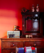 Close up of dark wood vintage furniture against a warm red decorated wall with trinket boxes and memorabilia in the bedroom