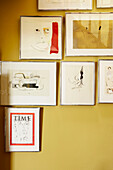 Framed artworks and drawings on a yellow wall