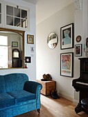 Gilt framed mirror above sofa in entrance room with artwork and piano