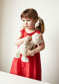 Junges Mädchen in rotem Kleid mit Teddybär in der Hand
