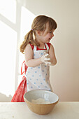 Young girl in red dress stands mixing flour in a bowl