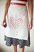 Low section woman in heart shaped apron holding red cupcakes