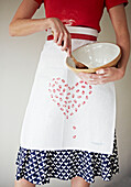 Low section woman in heart shaped apron holding a mixing bowl