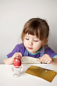 Kleines Mädchen klebt goldene Sterne auf ein gefärbtes Osterei
