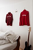 Bedroom detail with red sports shirts hanging on the wall and guitar
