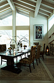 Dining table with upholstered chairs below high beamed ceiling in luxury Zermatt home, Switzerland