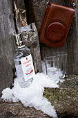 Bottle of vodka and glasses with brown camera case on fence in snow, Zermatt, Valais, Switzerland