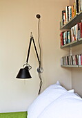 Wall mounted desk lamp with bookshelf in contemporary London bedroom, England, UK