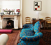Blaues blattgemustertes Sofa und beleuchtetes Feuer im Wohnzimmer eines alten Londoner Stadthauses, England, UK