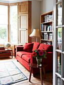 Red sofa and bay window in living room of colourful London home, England, UK