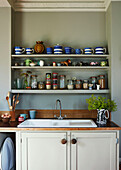 Storage jars and blue striped kitchenware on open shelving above kitchen sink in family home, Rye, East Sussex, England, UK