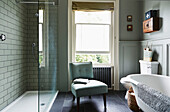 Glass shower screen with upholstered chair at open window in Rye family home, East Sussex, England, UK