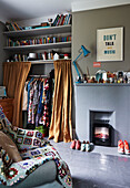 Clothes storage and shelves with crochet blanket on armchair in bedroom of Rye family home, East Sussex, England, UK