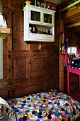 Wall-mounted cabinet above single bed with patchwork in wood-panelled Rye treehouse, East Sussex, England, UK