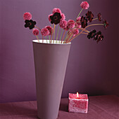 Nahaufnahme einer lilafarbenen Vase mit rosa Blumen und einer brennenden Kerze