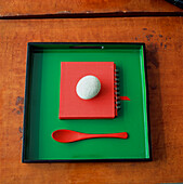 Orientalische Komposition aus Kieselstein auf rotem Notizbuch mit Löffel auf quadratischem, grün lackiertem Tablett