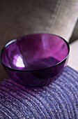 Tiefviolette Glasschale auf gewebtem Stoffüberwurf
