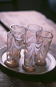 Set of five small coloured glasses with white streaked design on plate