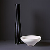 Tall black glass vase and white glass bowl on black background