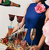 Woman holding an ornate tray of champagne glasses with man pouring from bottle