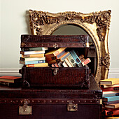 Vintage crocodile skin trunk and suitcase overflowing with old books with Rococo style gilt mirror in background