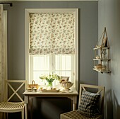 Window with shutters and floral roman blind with console table with white flowers and clothes brushes