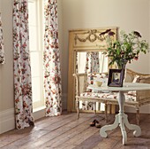 Pretty floral curtains and large mirror with cane chaise and round side table with fresh flowers