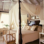 Four poster bed with swathes of cream fabric in sunlit room