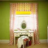 Oval mirror on dressing table at window with floral patterned curtains